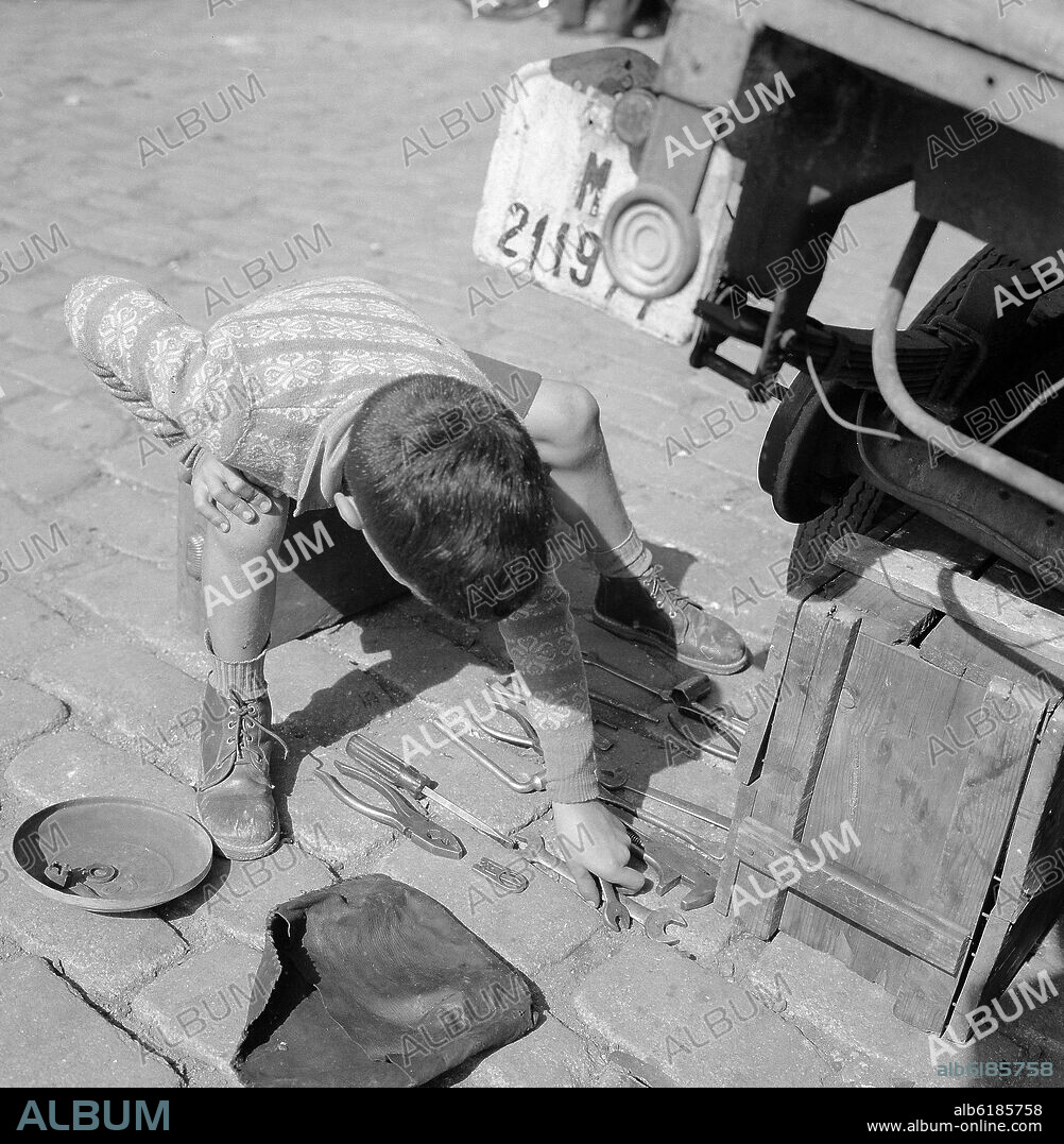 NIÑO COLOCANDO HERRAMIENTAS EN EL SUELO - FOTOGRAFIA EN BLANCO Y NEGRO - AÑOS 50.