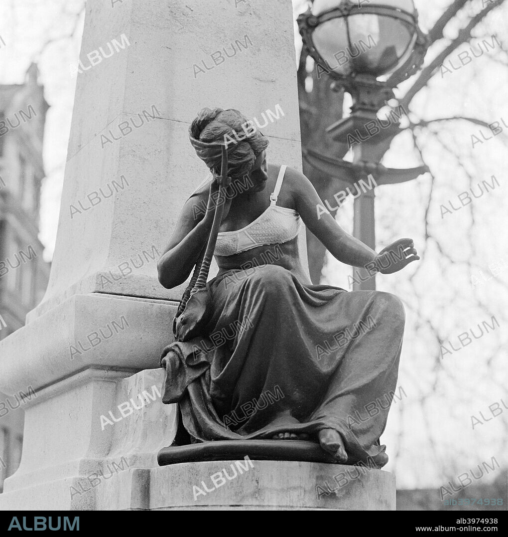 The Edward Onslow Ford Memorial wearing a bra, Abbey Road, St John's Wood, London, 1973. Memorial to British sculptor Edward Onslow Ford (1852-1901) featuring Ford's own 'Muse', a bronze seated female figure with a bra that someone has put on, with obelisk and lamp standard behind.