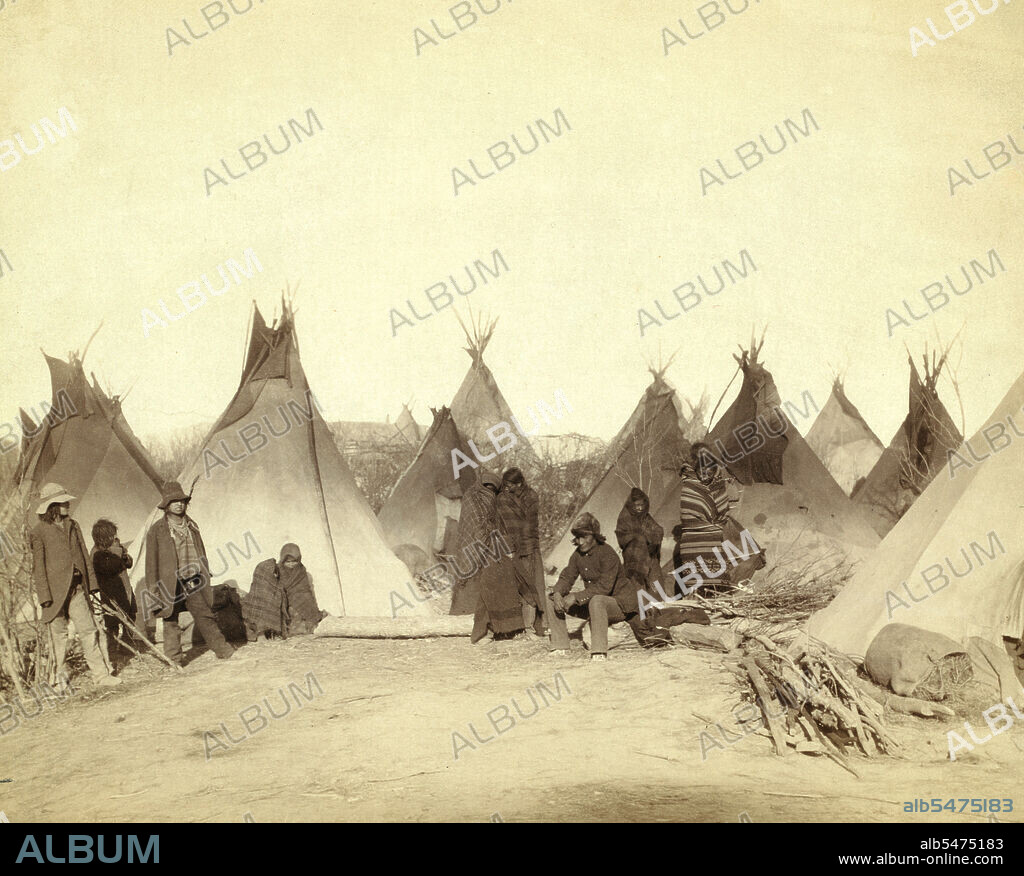 Group of twelve Miniconjou (children and adults)--many are looking away from camera--in a tepee camp, probably on or near Pine Ridge Reservation. 1891.