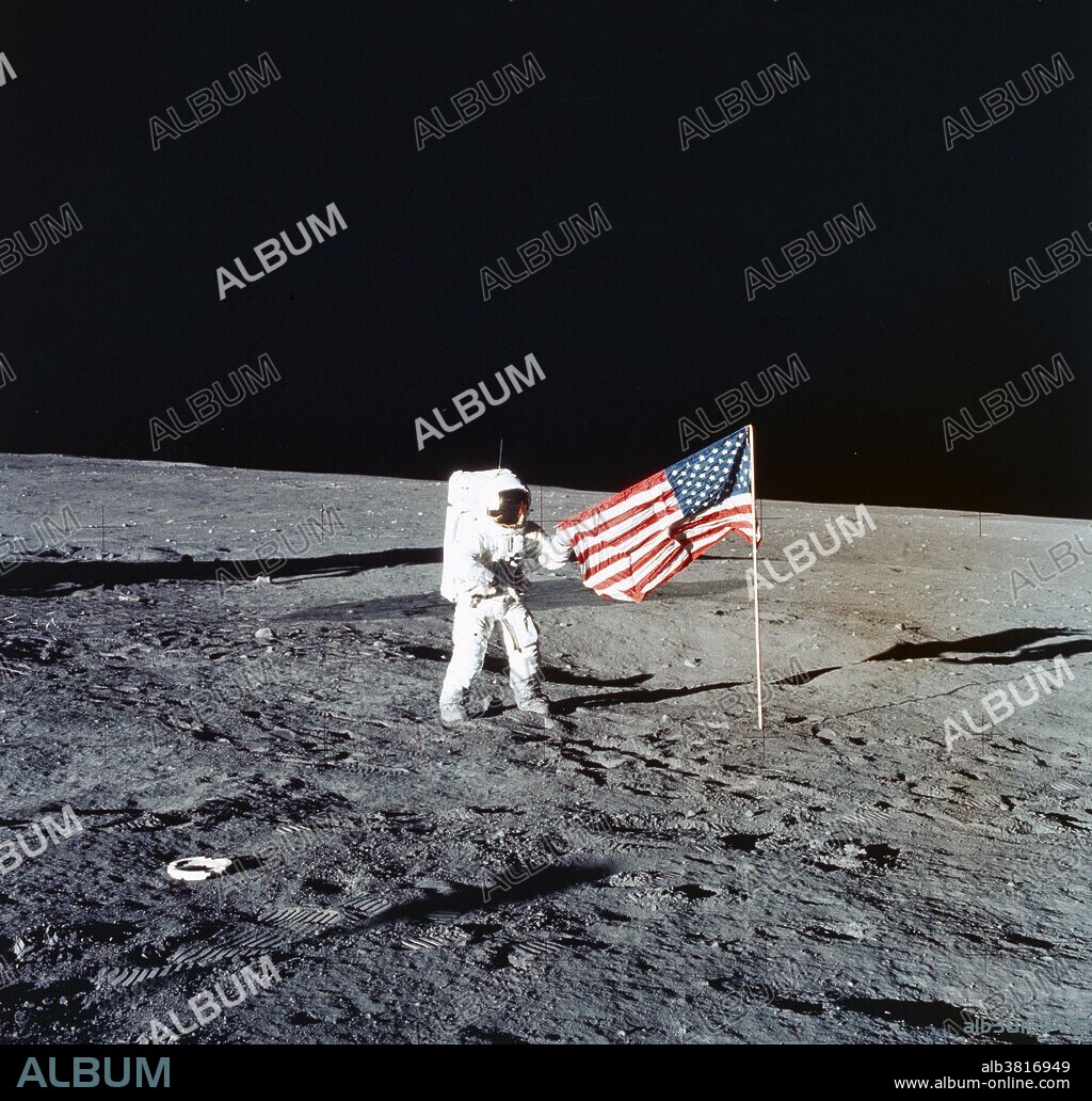 Astronaut Charles Conrad Jr., Apollo 12 commander, stands beside the United States flag after it was unfurled on the lunar surface during the first extravehicular activity (EVA), on Nov. 19, 1969. Several footprints made by the crewmembers can be seen in the photograph. While astronauts Conrad and Alan L. Bean, lunar module pilot, descended in the Lunar Module (LM) "Intrepid" to explore the Ocean of Storms region of the moon, astronaut Richard F. Gordon Jr., command module pilot, remained with the Command and Service Modules (CSM) "Yankee Clipper" in lunar orbit.