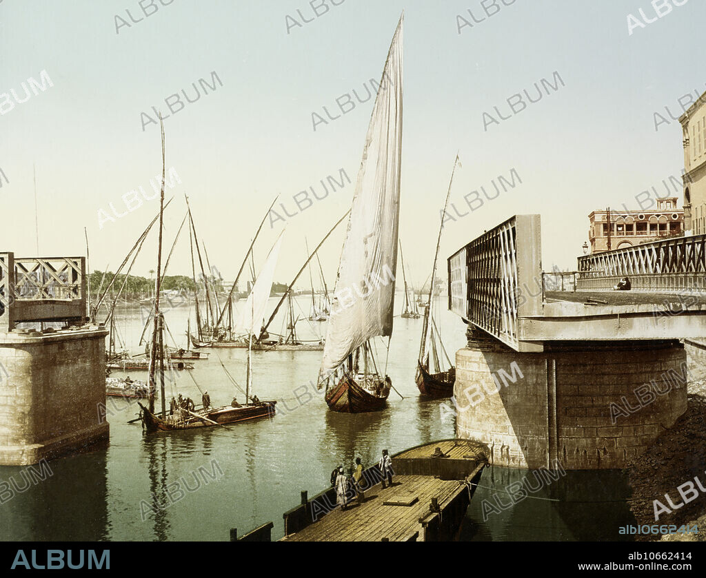 A photochromic print of Gezira bridge, Cairo, open for sailing ships to pass through it. Spanning the Nile River, Kobri el Gezira Bridge connected downtown Cairo to Gezira Island and the Zamalek district. Completed in 1871, the truss bridge lasted until the 1930s when it was replaced by the Qasr al-Nil Bridge. This image was made by French industrialist Paul Fleury. Photochrom (also called the Aac process) prints are colorized images produced from black-and-white photographic negatives via the direct photographic transfer of a negative onto lithographic printing plates. The process is a photographic variant of chromolithography, a broader term that refers to colour lithography in general.