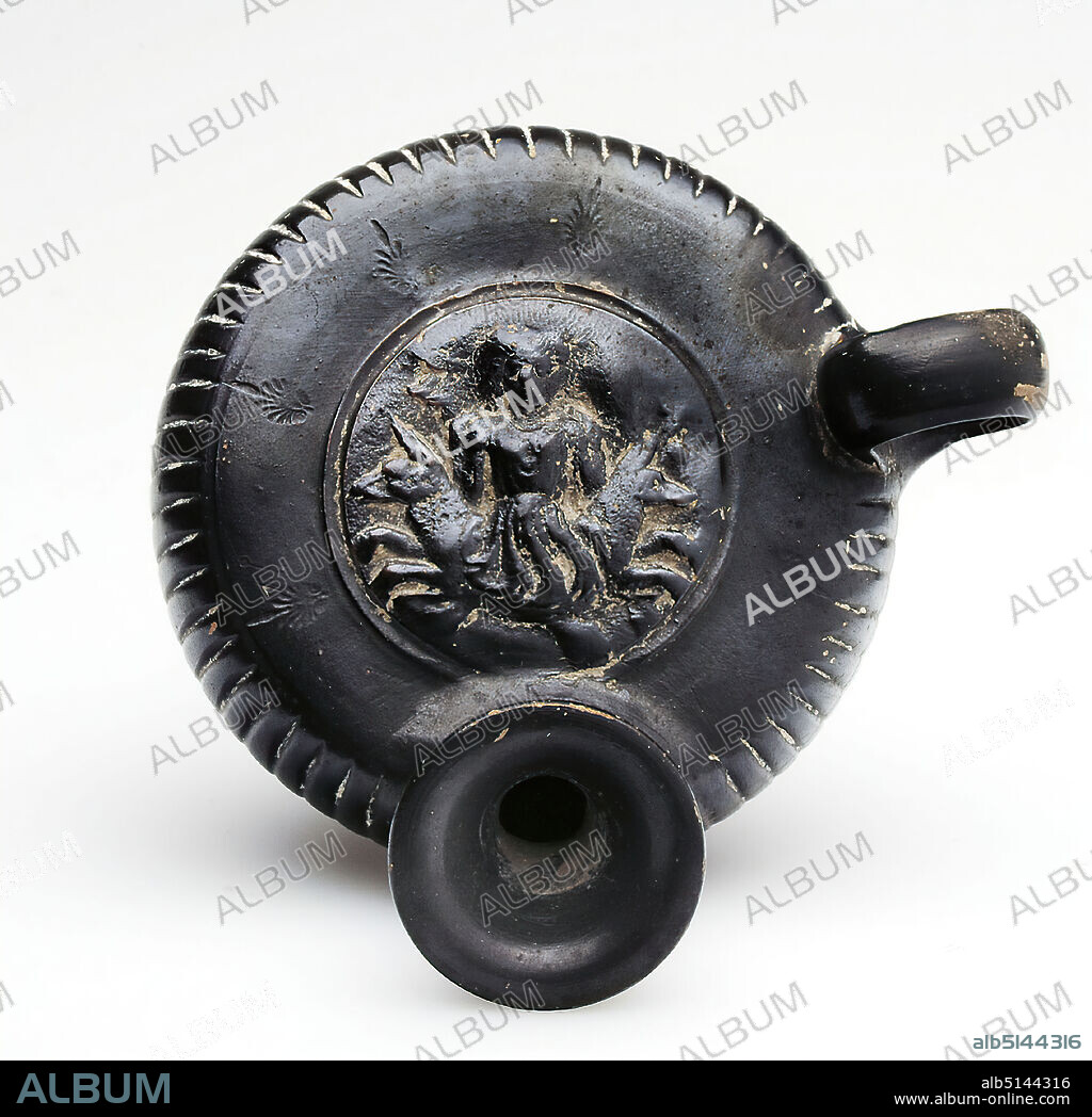 Guttus with stamped palmette ring (Skylla), Formerly Johannes W. F. Collection Reimers (Hamburg), clay, quickly turned, hand modeled, press decor, stamped, fired (ceramic), clay, Total: Height: 8.3 cm; Diameter: 9.5 cm; Base diameter: 6 cm; Width: 11.2 cm; Depth: 11.2 cm; Diameter: 4.7 cm (medallion); Height: 1 cm (stamped palmette), Pottery, Scylla (sea monster), Late Classic (Greek antiquity), Greek antiquity, The Guttus has a stocky shape, flattened at the top and bottom, with a profiled low foot, a vertical handle and a sloping spout. The body of the vessel is vertically grooved. On the flat top there is a medallion pressed with a mould. It depicts the sea monster Scylla. She is clothed with a belted chiton, has both arms angled to the side and her hands directed to her shoulder. The head with hair falling to the sides is shown in frontal view. To the sides, a wolf or dog front body emerges from her body, which once tore the sailors from their ships and devoured them. Left beside the head of the Scylla possibly a rest of the tail fluke is indicated. The medallion is surrounded by five stamped palmettes with a long lancet leaf; one is located between the handle and spout. Due to its flat shape and the vessel, which is covered with black luster down to the underside of the foot, it is an early Guttus.