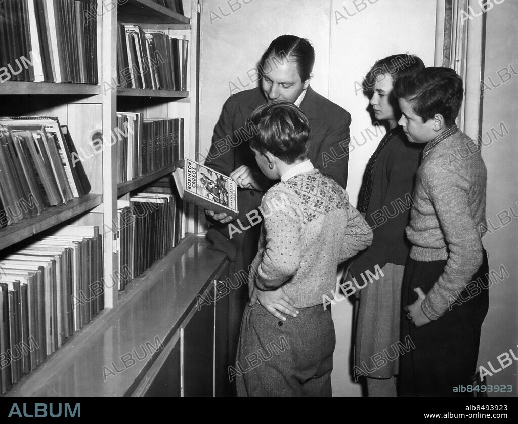 ARKIV 19511113. En bibliotekarie håller upp boken "Robinson Kruse" för några ungdomar på ett bibliotek i Sverige 1951.. Foto: Tore Falk / XP / SCANPIX / Kod: 1048. **AFTONBLADET OUT**.