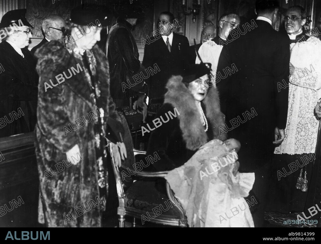 Roma, 26/1/1938. Bautizo del futuro Rey Juan Carlos I. La Reina Victoria Eugenia, con su ahijado en brazos. Don Juan (de espaldas) conversa con el Cardenal Pacelli (futuro Pío XII) que fue quien le impuso el bautismo. Al fondo, Alfonso XIII.