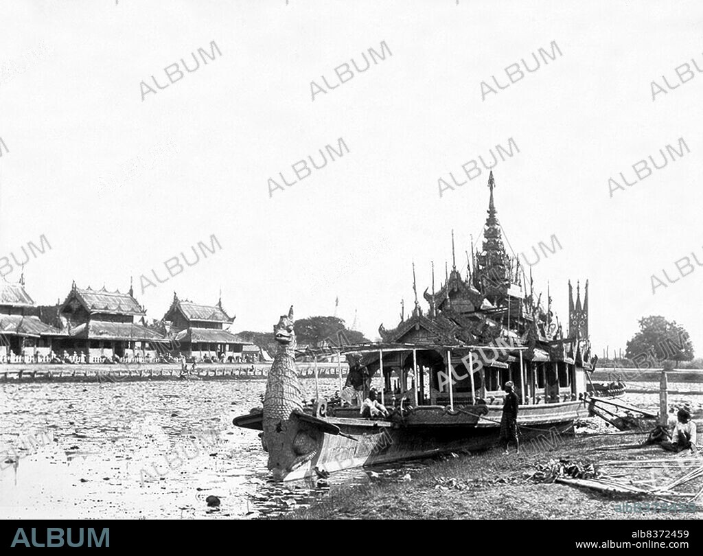 The photograph is from a series documenting the Third Anglo-Burmese War (1885-86) made by Hooper while serving as Provost Marshal with the British army. Thibaw was the last king of Burma and ruled from 1878 until 1885, when he was deposed and exiled to India by the British. The Burma Expeditionary Force entered Mandalay, the Burmese royal capital, on 28 November, beginning an occupation of the city, and the war culminated in the annexation of Upper Burma by the British on 1 January 1886.<br/><br/>. Burmese state barges were magnificent gilded vessels roofed by a tiered spire (pyatthat) denoting sacred royal space, and a prow in the form of a mythical beast or celestial spirit. They were used by kings, courtiers and high officials in spectacular ceremonial processions and water festivals. At Mandalay the barge was moored on the moat which surrounded the city.<br/><br/>. Hooper describes the barge and the use to which it was put during the occupation in a caption accompanying the photograph: 'This is a very gorgeous affair, the whole of it is gilded over, and it has a wonderful looking prow in the form of an eagle. The usual bits of looking glass have not been omitted in its decoration. Theebaw and his Queen used to be towed round the moat in this, on some of the rare occasions when he ventured out of the palace enclosure. It is now moored alongside the berm near the northeast corner of the city, where the 'Gymkhana' sports of the Garrison are held, and serves as a refreshment room, a very necessary adjunct to any athletic sports in the tropics'.