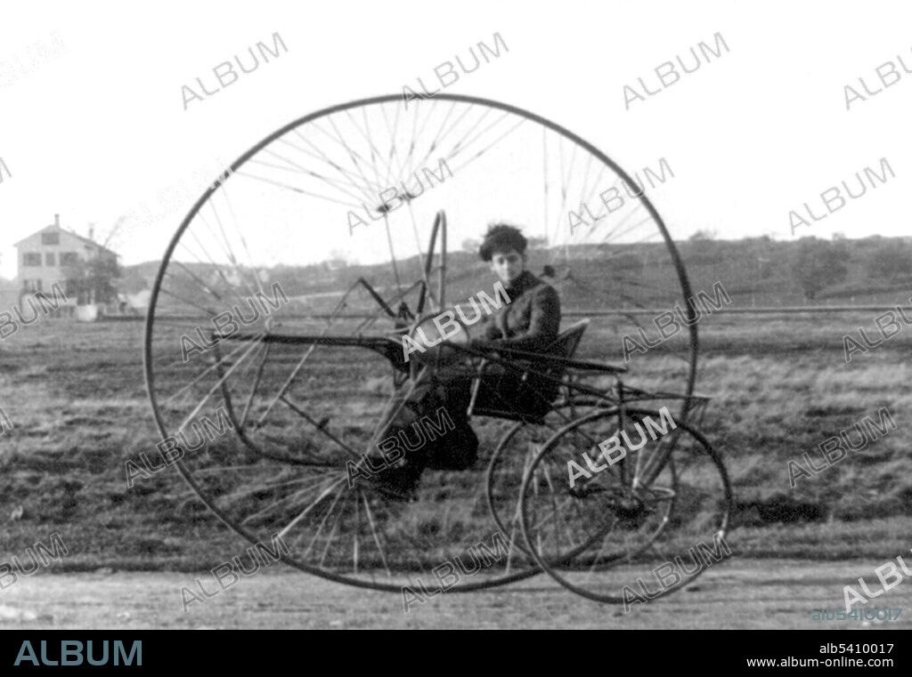 View of Charles Oldreive's new tricycle; the New Iron Horse, with a lady inside. In 1876, James Starley developed the Coventry Lever Tricycle, which used two small wheels on the right side and a large drive wheel on the left side; power was supplied by hand levers. In 1877, Starley developed a new vehicle he called the Coventry Rotary, which was one of the first rotary chain drive tricycles. By 1884, there were over 120 different models produced by 20 manufacturers. Tricycles were used by riders who did not feel comfortable on the high wheelers, such as women who wore long, flowing dresses. Photographed by Charles Wood Oldreive, 1882.
