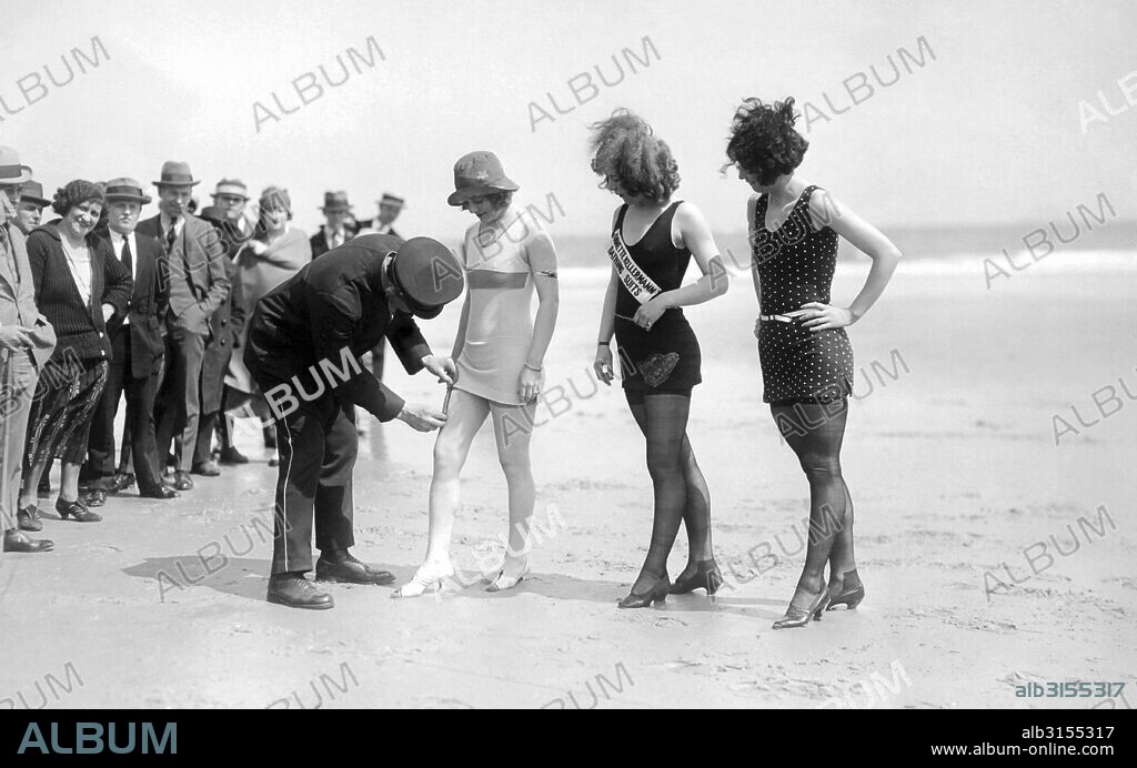 Atlantic City, New Jersey:  c 1921. A dubious and curious police officer measures the hem of the newest in bathing fashions. Are the suits decent?  Time will tell!.
