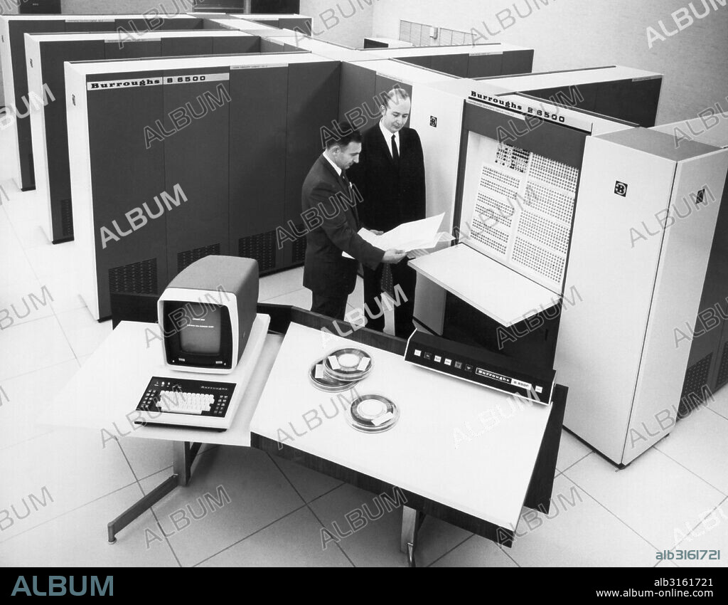 United States: 1969 Burroughs Corporation computer systems specialists review a print-out at the maintenance diagnostic display model of the new B6500 computer system.