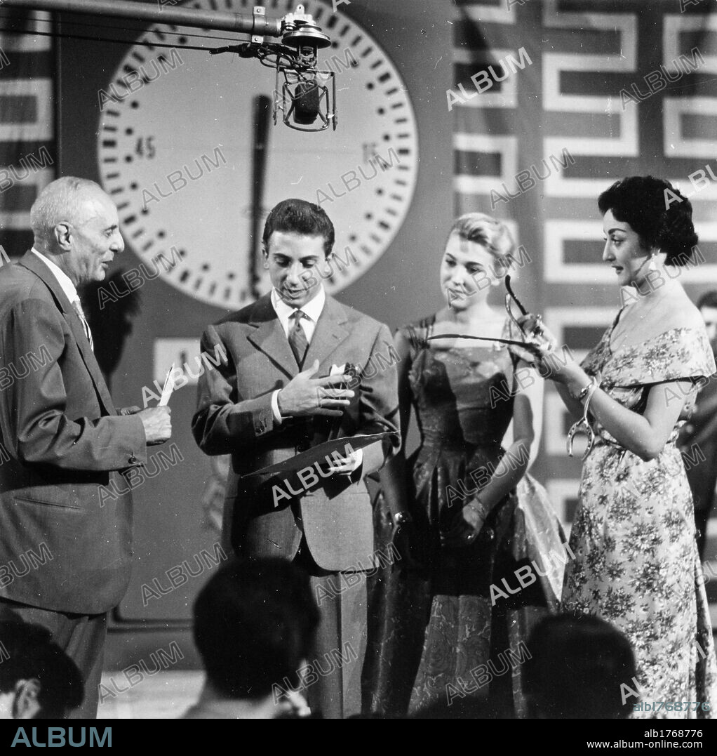 Mike Bongiorno presenting 'Lascia o raddoppia? ' ('Take it or leave it'). The Italian American presenter Mike Bongiorno reading a question to the competitor Maria Luisa Garoppo during the recording of the television programme  'Lascia o raddoppia?', presented with his assistant Edy Campagnoli. Milan, 1956.