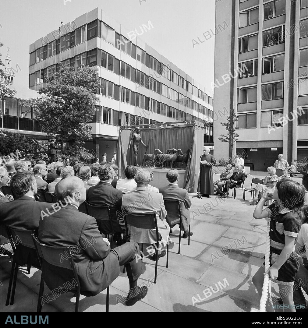 DAME ELISABETH JEAN FRINK. Paternoster Square, City of London, 30/07/1975. Guests listening to a speech during the unveiling ceremony for the bronze sculpture of a shepherd and sheep by Elisabeth Frink at the Paternoster development. Work on the Paternoster development in the 1960's was carried out in a joint venture by John Laing Construction Limited, Trollope and Colls Limited, and George Wimpey and Company Limited. The development consisted of a series of office blocks, a shopping precinct, an extensive piazza and a three-level car park.In July 1975, a bronze statue of a shepherd and his sheep, sculpted by Elisabeth Frink, was unveiled at the Paternoster development by the world famous violinist Yehudi Menuhin. The sculpture was commissioned by Paternoster Development as their contribution to European Architectural Heritage Year. Among those present at the ceremony were Sir Kirby Laing and Geoffrey Anderson, then managing director of the Development company.