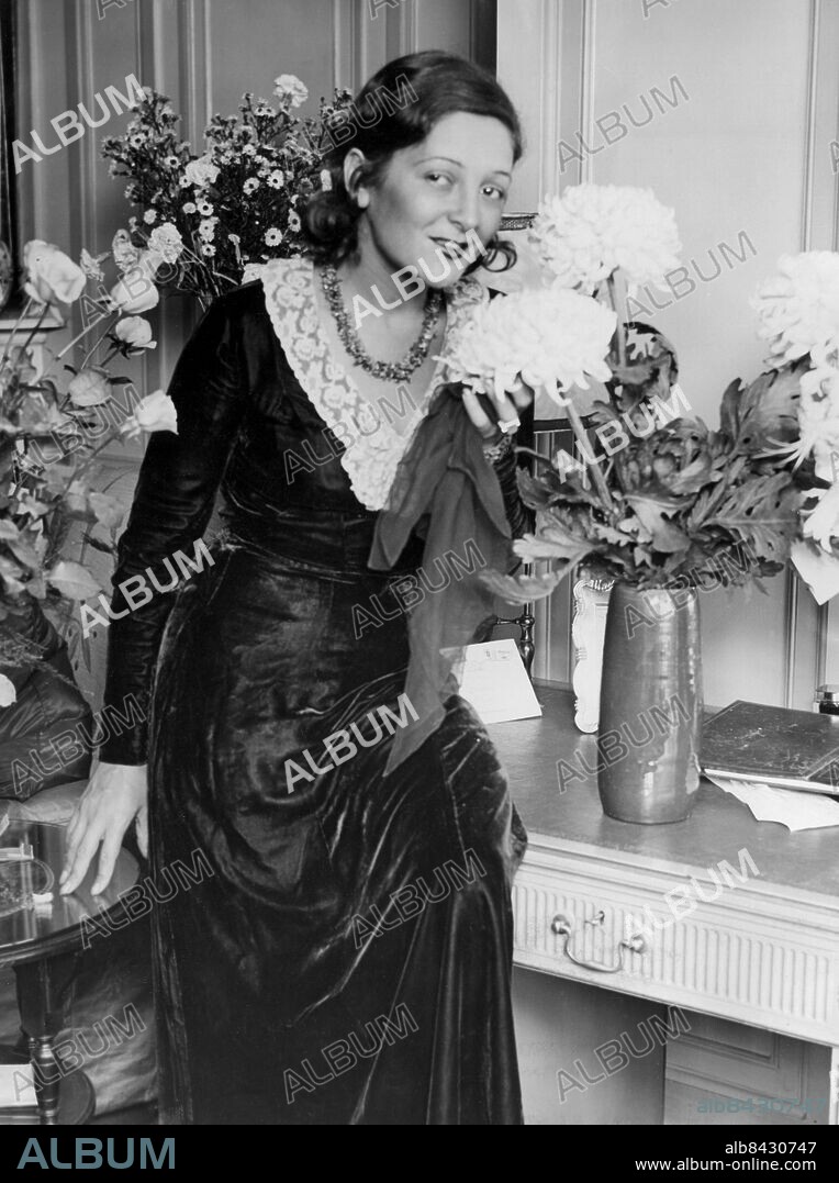 Orig. bildtext... MISS LYA DE PUTTI SETS A NEW FASHION. Miss Lya de Putti, the world famous Film Star who is soon to make her debut on the West End Stage, sets a new fashion - wearing a heel-length black velvet dress ornamented with a lace collar. O.P.S. Miss Lya de Putti arranging the flowers of welcome in her hotel in London today. 20/9/29 Orig. bildtext... MISS LYA DE PUTTI LANCERAR ETT NYTT MOD. Här ovan synes Miss Lya de Putti, de världsberömda filmstjärnan, som snart skall göra sin debut på West End Stage, lancerande ett nytt mod - lång svart sammetsklänning med spetskrage. Fotot är taget på hennes hotell i London strax efter hennes ankomst dit. Orig. bildtext... (...)A DE PUTTI Not. Lya de Putti Anm. L de Putti, 1899-1931, ungersk stumfilmsstjärna, verksam i Tyskland och USA. Klänningar Långklänningar Spetskragar Kragar Vaser Halsband Buketter Leende Läppstift Smink Sammet Lansering CD559 persons: LYA DE PUTTI sites: UNGERN*;LONDON;STORBRITANNIEN.