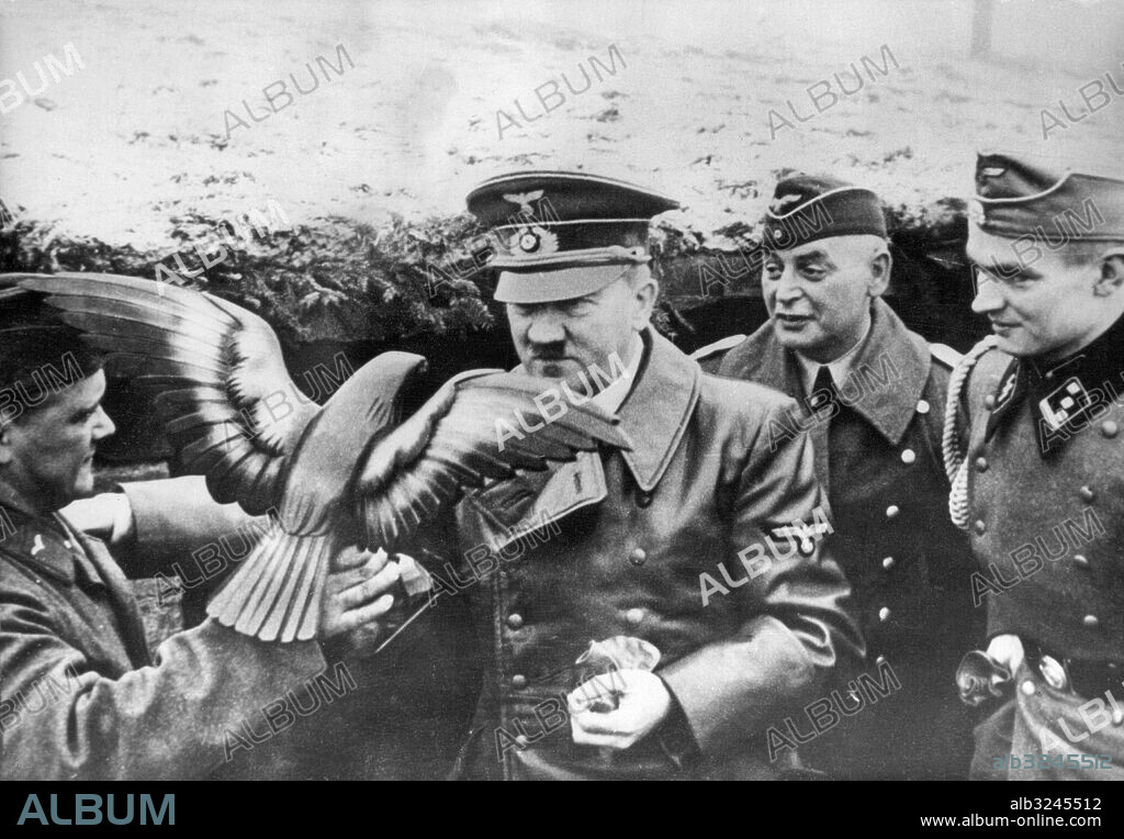 Orig. bildtext... HITLER, IT SEEMS, HAD A VERY MERRY CHRISTMAS AT THE FRONT. The latest issue of the Schwarze Korps, organ of the Nazi SS Guards, gives details of Hitler's Christmas visit to the western front and recounts a story of extravagance calculated to cause much heartburning in German homes where the festival was marred by insufficient food and fuel. Photo shows:- Hitler receiving a wooden eagle from a soldier who carved it himself, during his visit to the western front. Anm. A Hitler, 1889-1945, tysk-österrikisk politiker, Tysklands Führer och diktator 1934-1945. Mustascher Uniformsmössor Symboler Örnar Träfigurer Presenter Gåvor Knappar Läderjackor CD556 persons: ADOLF HITLER sites: TYSKLAND PhotoDate:194?-??-??.