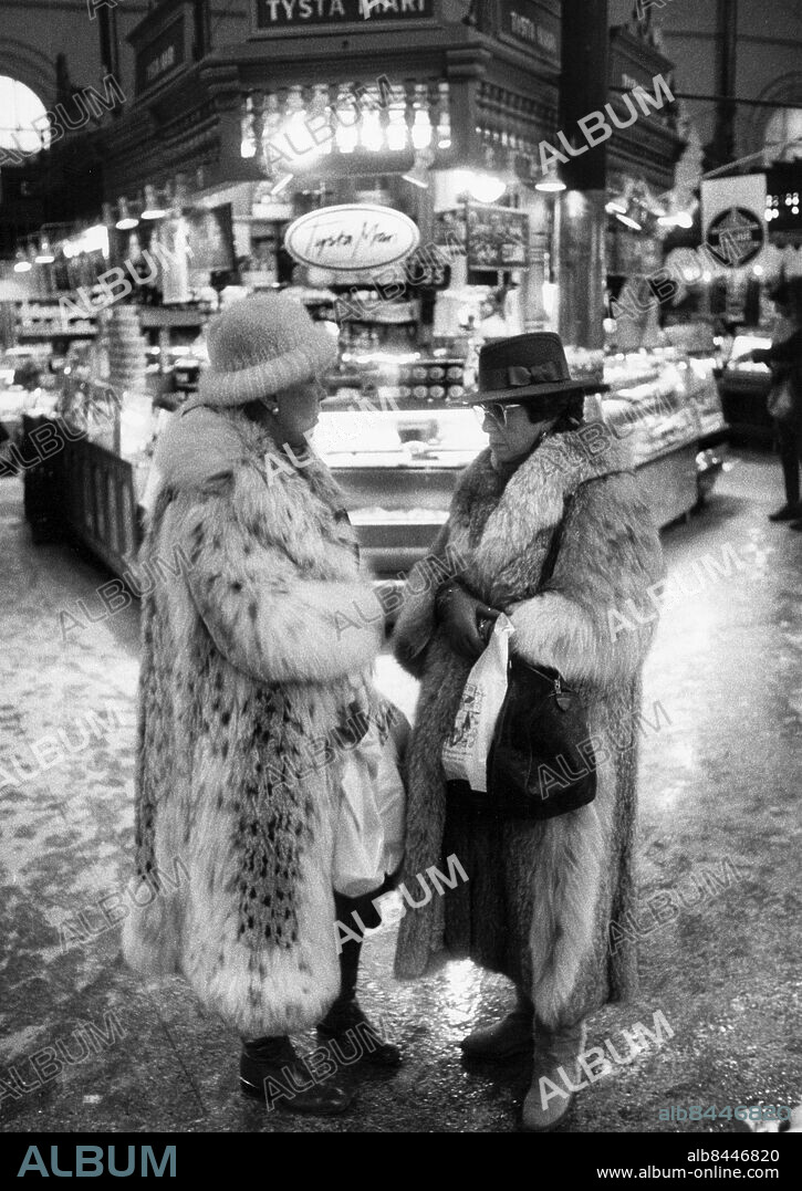 STOCKHOLM 1985-01-01. I Östermalmshallen träffas man för att handla delikatesser, byta rykten och synas. Två kvinnor i pälskappor framför Tysta Mari. Foto: Björn Lundberg / Expressen / TT / Kod: 80. ** AFTONBLADET OUT **.