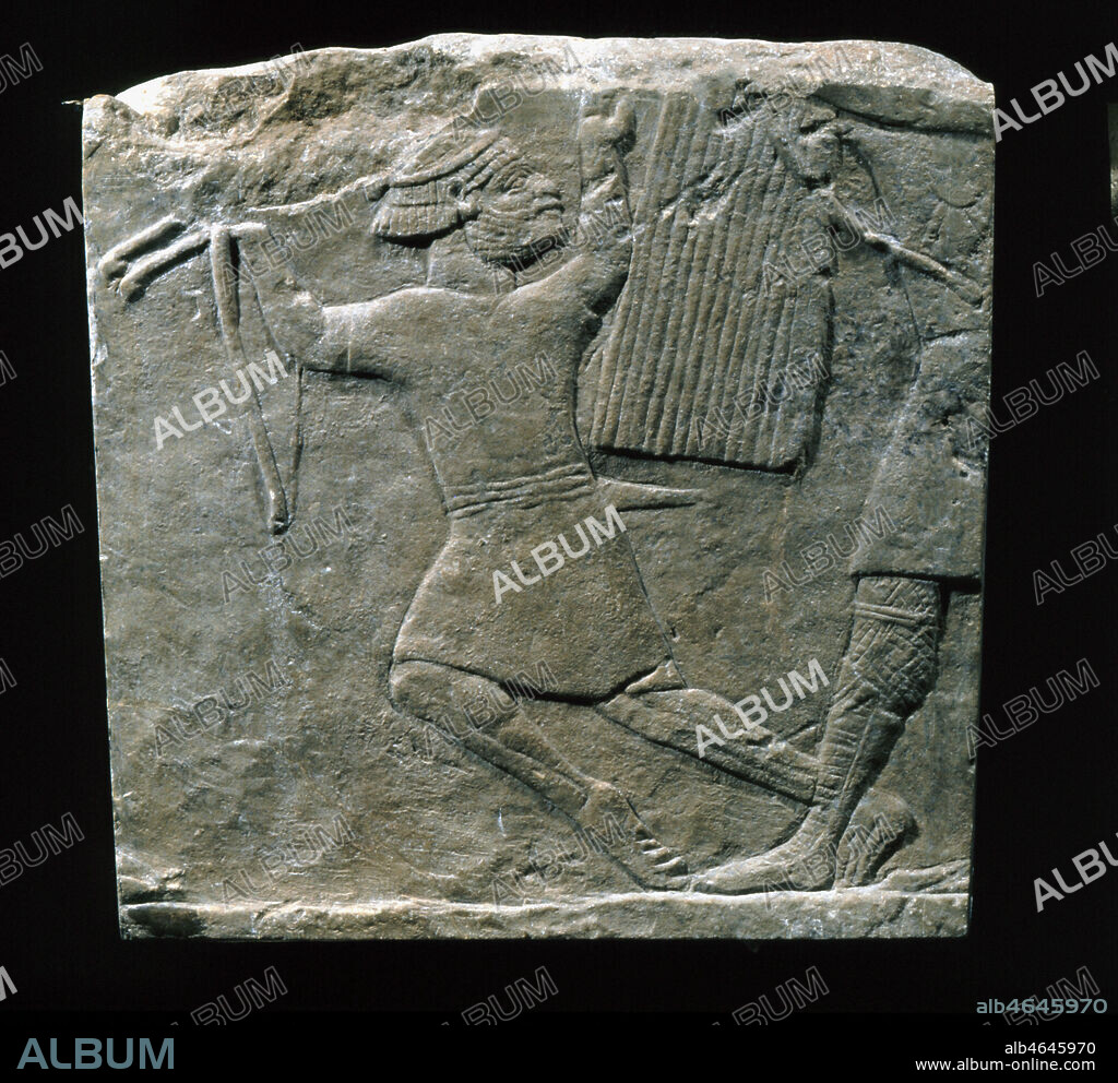 Fragment de bas-relief en albâtre gypseux : guerrier ennemi tombant devant un soldat. Vers 645-640 av. JC. Provient de la ville de Ninive, ancienne capitale de l'Assyrie en Iraq actuel.. L'archer qui s'effondre sous les coups d'un soldat est aisément identifiable par sa coiffure. Un bandeau posé sur ses cheveux traités en deux rangées de mèches courtes, est noué à l'arrière de la tête : c'est un élamite. Il semble très peu protégé des coups par rapport à l'équipement de son adversaire. Il ne porte qu'une tunique courte sans cuirasse, et il combat les pieds et les jambes nus. Credit : Larrieu-Licorne/Kharbine-Tapabor.