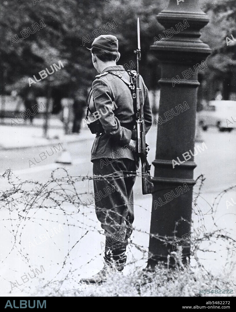 Berlin Wall Photo -  August 1961 - Standing Like A Forlorn Symbol of Repression, This Teen-Aged East German Soldier Stand Guard By The Closed Border.