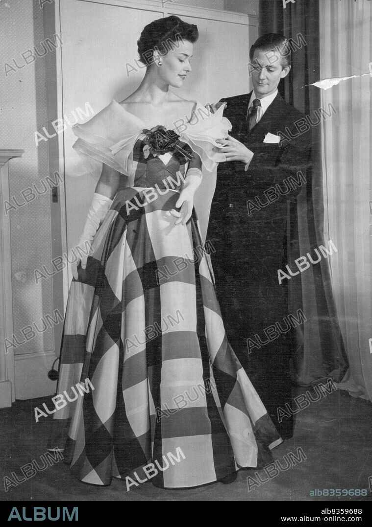 Australian Joins London's Fashion Leaders -- Robert Schulz adjusts one of his latest creations entitled 'Pierrot'. It is a check raw silk evening gown with full skirt over organza petticoat. It has eight large organza collars caught in front with red roses.First Australian to open a haute couture house in Britain is Robert Schulz, born at Booleroo, South Australia, in 1924.He decided at an early age to make dress designing his career and left Australia in 1947 to come to London. January 20, 1953. (Photo by Reuterphoto).