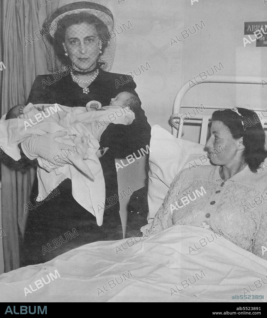 Duchess of Kent and The Babies - H.R.H. the Duchess of Kent (seen wearing the latest of hat fashions) nurses the twin girls Lesley and Norma, daughters of Mrs. Chandler, seen in the picture.H.R.H. the Duchess of Kent paid a visit to the Queen Charlotte's Maternity Hospital, Shepherds Bush, where she mad a tour of the wards and chatted to some of the mothers. April 12, 1946. (Photo by Fox Photos).