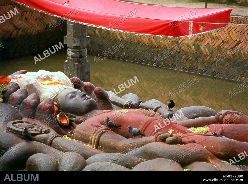 The Vishnu figure of Budhanilkantha is a 4.5 metre long, intricately carved figure depicting Vishnu sleeping on the ground of the cosmic ocean, on a 'bed' of intertwining snake bodies, which are all part of the eleven-headed giant snake Ananta, 'The Endless One'.<br/><br/>. The figure probably originated in the 7th century and is hewn out of a single piece of rock. According to legend, Budhanilkantha was discovered by a farmer while ploughing his field; the plough snagged on the figure, which was buried underground, and, to the farmers great surprise, the figure began to bleed. Budha means 'mud' and Nila-kantha is 'Blue Throat'; Budhanilkantha is regarded as a manifestation of Vishnu (not to be confused with a better known incarnation of Vishnu as Nilakantha).