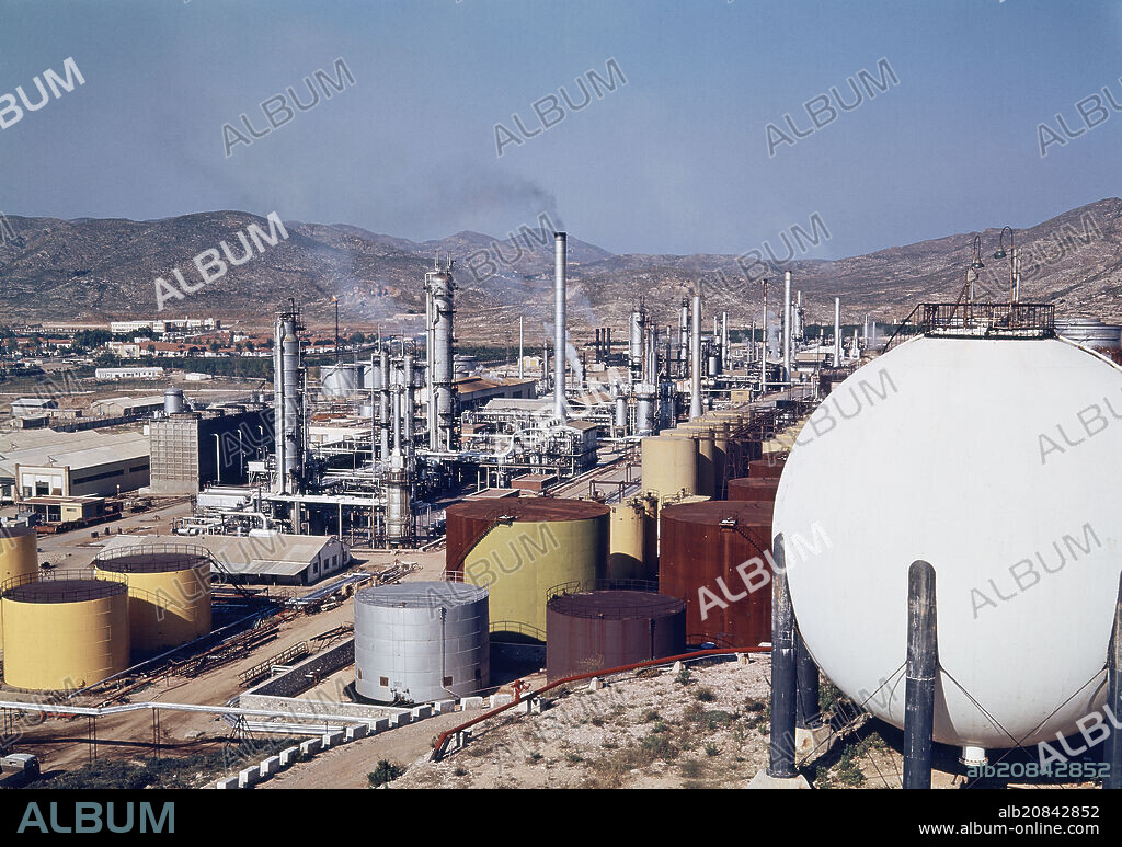 COMPLEJO INDUSTRIAL CON DEPOSITOS DE GAS Y COMBUSTIBLE Y CHIMENEAS CON EL ANTIGUO POBLADO DE ESCOMBRERAS AL FONDO - FOTO AÑOS 60.