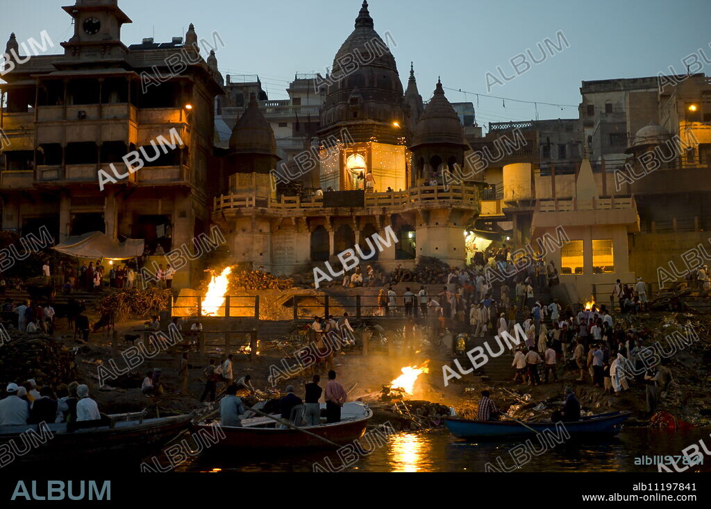 Tourists watch body bathed in River Ganges and traditional Hindu cremation on funeral pyre at Manikarnika Ghat in Holy City of Varanasi, Benares, India.