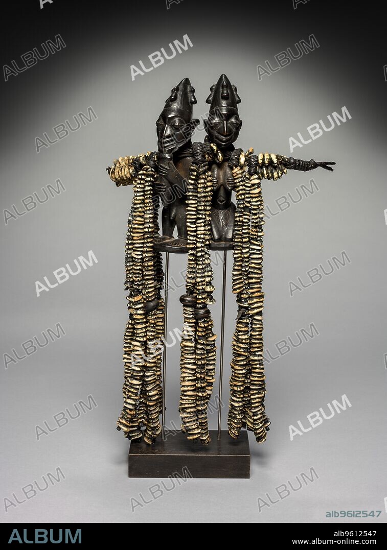 Eshu Dance Staff, 1800s. Eshu (also called Esu or Elegba) embodies the most complex deity in the Yoruba pantheon of gods. The messenger of the Yoruba gods, Eshu is also the bearer of sacrifices, guardian of the ritual way of life, and is associated with highly significant places including crossroads, markets, and home entrances. As seen here, Eshu’s power is often visually represented in  ogo elegba  (a male and female pair), referencing his ability to switch between the two genders, turn death into life (through childbirth), and to overcome the tension between the sexes. The male character bears a ritual flute reserved for this god. The abundance of cowrie shells means that Eshu brings wealth.
