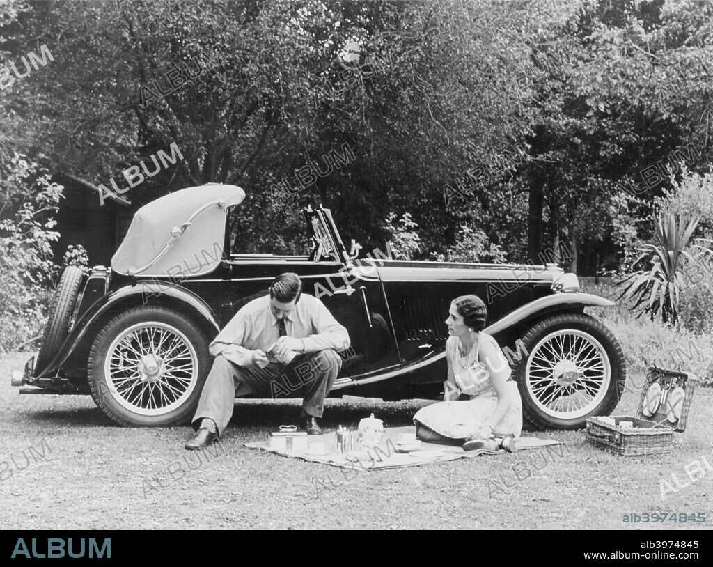 Couple having a picnic by an MG TA Midget, late 1930s. Introduced in 1936, the 1292cc TA Midget widened the appeal of sports cars, being less temperamental and easier to drive than its predecessors.