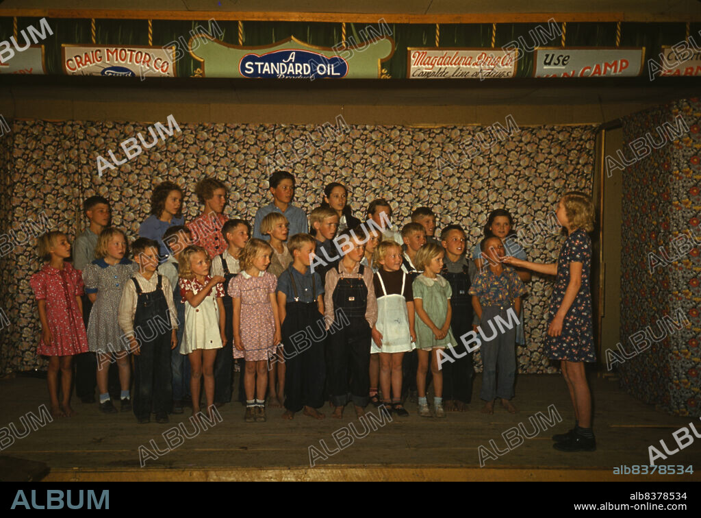 RUSSELL LEE. School children singing, Pie Town, New Mexico. [Signs: 'Craig Motor Co.; A Standard Oil product; Magdalena Drug Co. Complete line of drugs'].