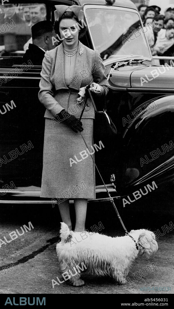 And Johnny Went Too: Royal Family Fly To Balmoral -- The dog runs around on a lead held by Princess Margaret, who wears an off-the-face hat with a two-piece grey costume. With 'Johnny,' a small white Sealyham, the Princess was waiting to board an aircraft at London Airport to fly with the King and Queen to Dyce airfield, near Aberdeen, to spend a Whitsun holiday at Balmoral. May 13, 1951.