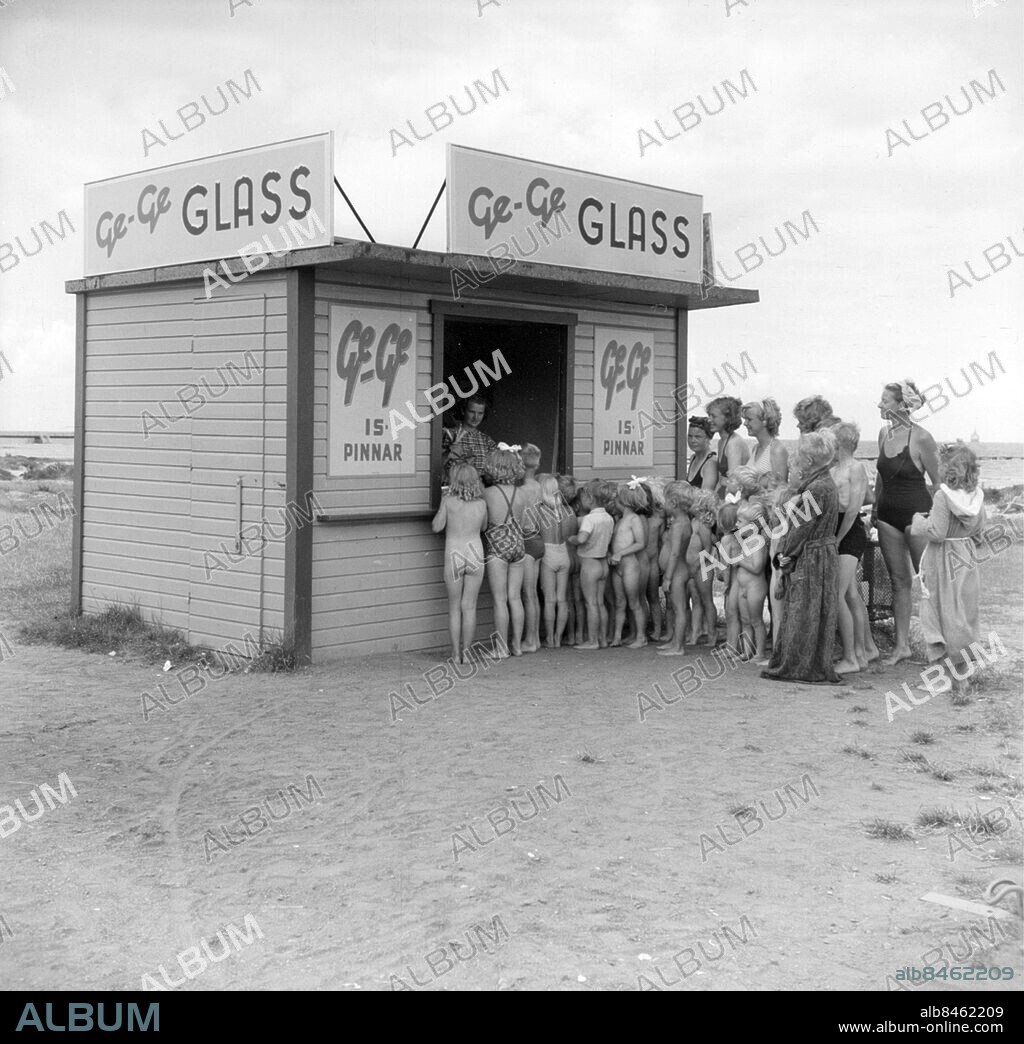 Glassförsäljning från kiosk vid Ribergsborgs friluftsbad, Ribban, Malmö sommaren 1949 . GeGe Glass (Malmö Glass Ab) ägt av Skånemejerier -ingår nu i GB-glass Foto: Bertil Rubin / Sydsvenskan /IBL Bildbyrå *** Local Caption *** barn mammor kö skyltar badrock naken nakna. ivsmedel glass Glasskö sommar glassförsäljning Malmö befolkning. Malmö Handel kiosker glasskiosk Bad Ribersborg. Företag GeGe glassbaddräkt sommar . L.