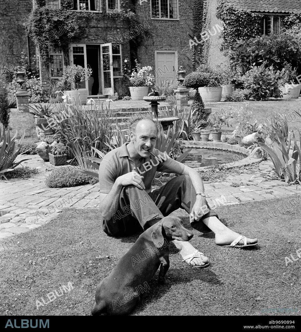 Artist Edward Seago in the garden of his home - The Dutch House at Ludham in Norfolk with his dachshund called Chaucer. June 1954.