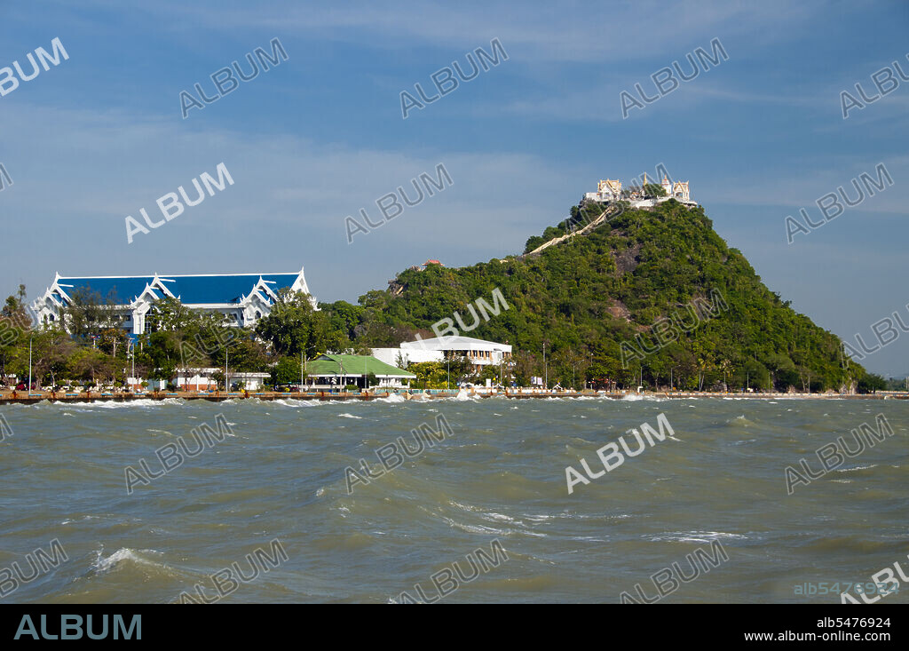 Prachuap Khiri Khan means town among the mountain chain. Although little more than a fishing port, the town which, depending on who you speak to, is either the last provincial capital in Central Thailand, or the first provincial capital in the south has a distinct charm to it, and is well off the beaten tourist track. That is, tourists pass through all the time, but they rarely stop. In historical terms, Prachuap is significant as one of the seven landing points where Imperial Japanese troops stormed ashore in 1941, on their way south to occupy Malaya and Singapore. Today, however, the town is a pleasant, laid-back fishing port with colorfully-painted fishing vessels at anchor in the harbor and an attractive waterfront walking street with some very good and reasonably priced restaurants. These aside, there is no nightlife worth speaking of. The town is ringed on the land side with rugged limestone mountains, one of which Khao Chong Krajok, or mirror tunnel mountain is pierced with a natural opening that appears not unlike a giant mirror, and which is perhaps the towns most famous natural landmark. Perched atop Khao Chong Krajok, high above the town, and at the top of a long flight of stone stairs, a revered temple called Wat Thammikaram serves as Prachuaps most revered site, and offers besides spiritual enlightenment fine views across the town and the bay.