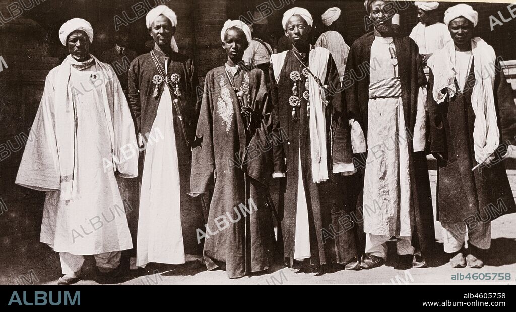 Sudan, Printed caption reads: 'Gimma Sheikes, Blue Nile. Published by G N Morhig, The English Pharmacy, Khartoum. Copyright 109'. Six Gimma 'sheikhs' pose for a group portrait. They wear traditional dress including 'thobs' (ankle-length garments with long sleeves), 'bishts' (loose-fitting outer cloaks) and turbans, [c.1906]. 2003/222/1/2/85.