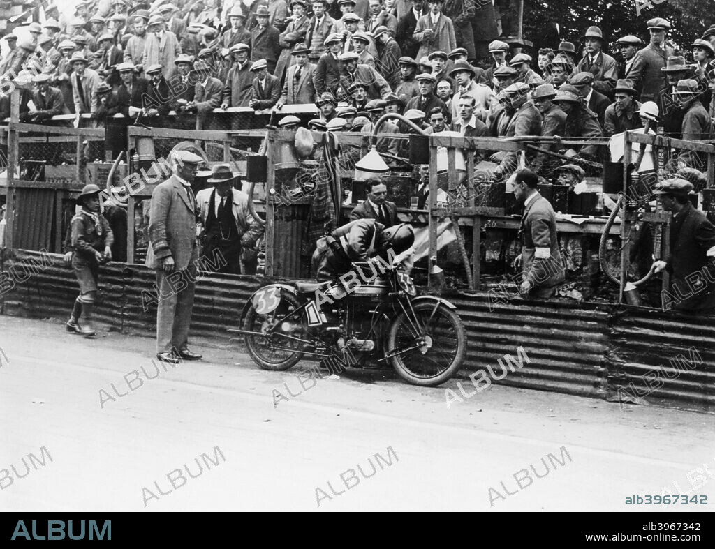 Alec Bennett at the Senior TT, 1924. Refuelling his Norton bike at the edge of the track. The spectators above him watch as he does so. A Boy Scout can be seen on the left.