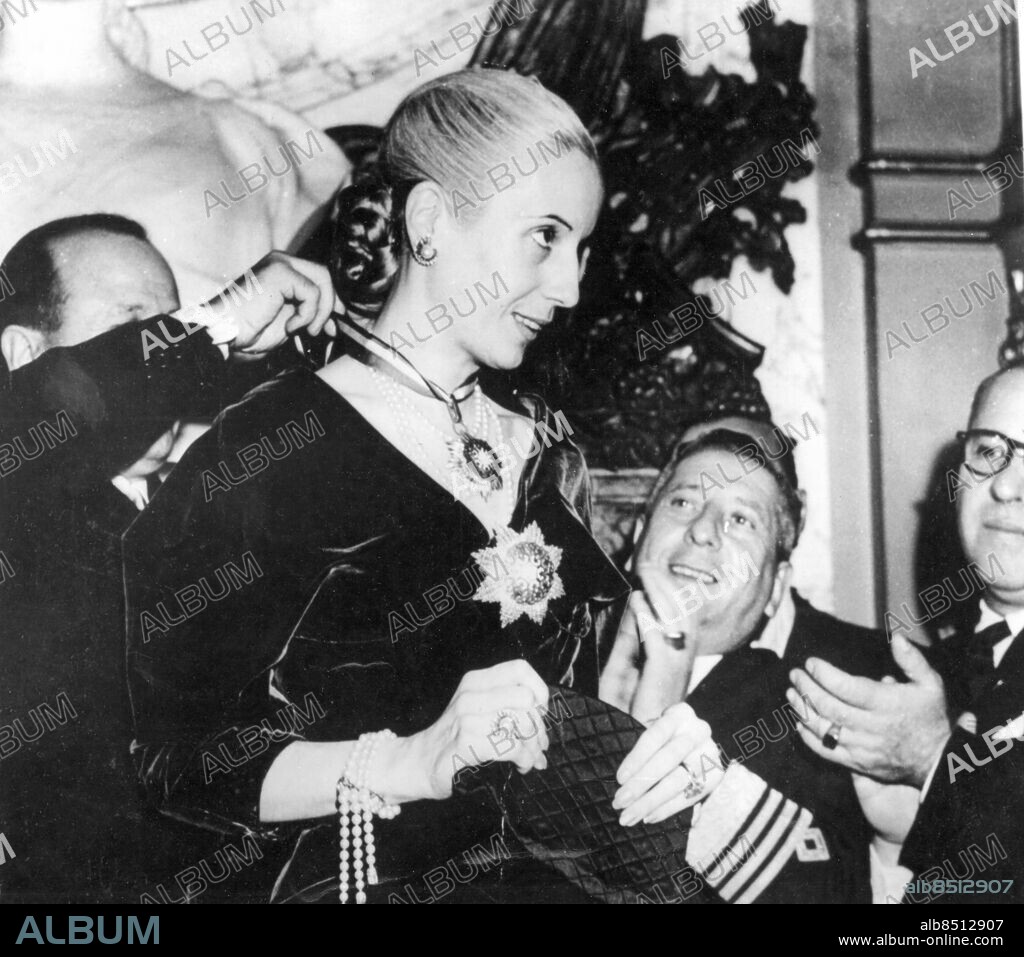 Orig. bildtext... NEW HONORS FOR EVA PERON--BUENOS ARGENTINA Mrs. Eva Peron, attractive wife of Argentinas president Juan Peron is shown being decorated with the Omeyades order during a recent ceremony in Buenos Aires. A member of the syrian delegation in Argentina is attaching the ribbon of the order around Mrs. Peronós neck as he made the presentation in his countryós name. Anm. Utmärkelser Profiler Klappar händerna Örhängen Armband Broscher CD455 persons: EVA EVITA PERON sites: SYRIEN*;BUENOS AIRES;ARGENTINA.