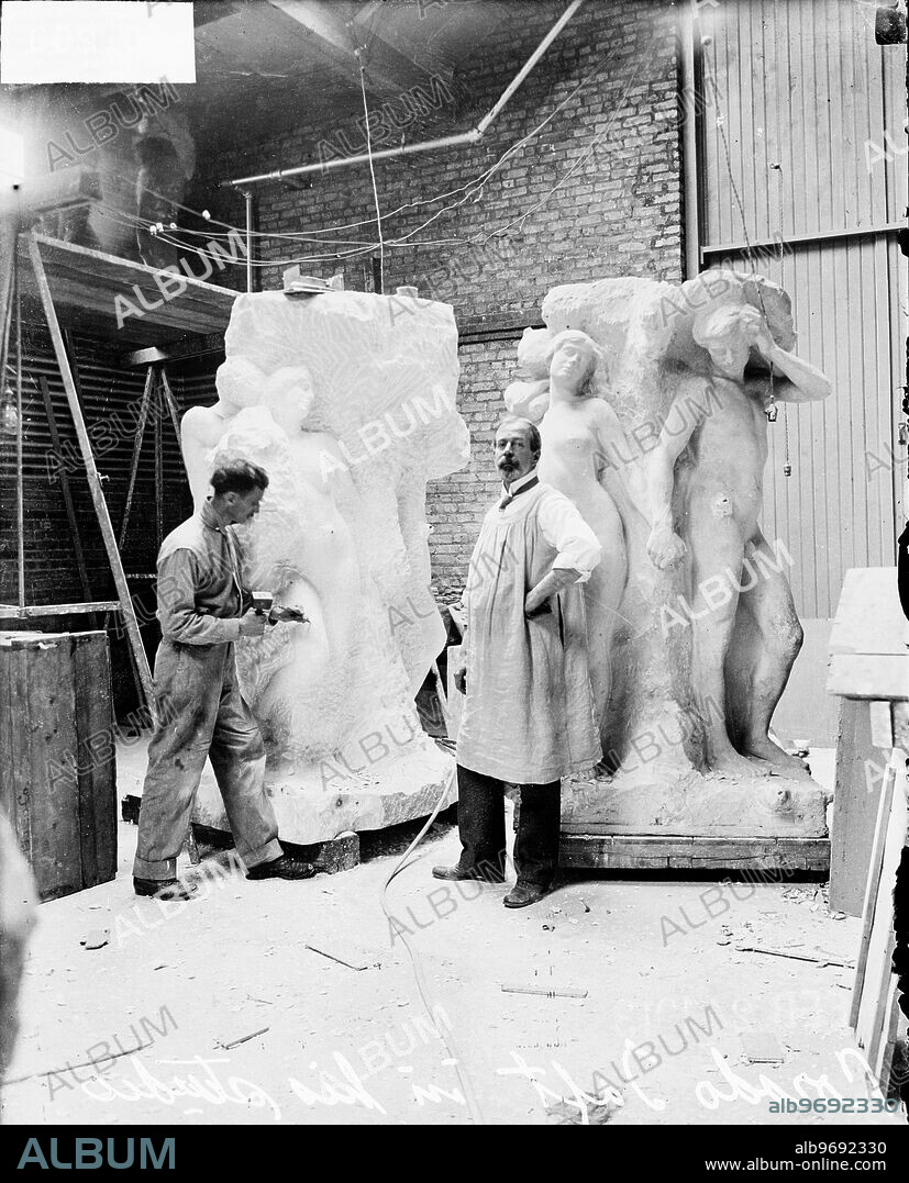 Portrait of sculptor Lorado Taft, wearing a smock, and stone carver Walter Zimmerman, using a hammer and chisel on a sculpture, at work on the Solitude of the Soul sculpture in Taft's studio on South Ellis Avenue in the Hyde Park community area of Chicago, Illinois. The sculpture is in the collection of the Art Institute of Chicago.