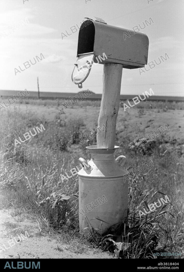 Entitled: "Mail box set up in milk can near Hydro, Oklahoma." Before the introduction of rural free delivery (RFD) by the Post Office in 1896, many rural residents had no access to the mail unless they collected it at a post office located many miles from their homes or hired a private express company to deliver it. For this reason, mailboxes did not become popular in rural America until curbside RFD mail delivery by the Post Office was an established service. In 1923 did the Post Office finally mandate that every household install a mailbox or mail slot in order to receive home delivery of mail. Originally designed only for incoming mail delivery, curbside mailboxes were soon fitted with a semaphore or signal flag mounted on an attached arm to signal the postman of outgoing mail, but also by the postman to inform the recipient that incoming mail had been delivered - a convenience to all during periods of freezing or inclement weather. Curbside mailboxes located on a rural route or road and sited at the intersection of the road with each recipient's carriageway or private drive allowed limited numbers of mail carriers to deliver mail to many widely scattered farms and ranches in a single day. Photographed for Farm Security Administration by Russell Lee, 1939.