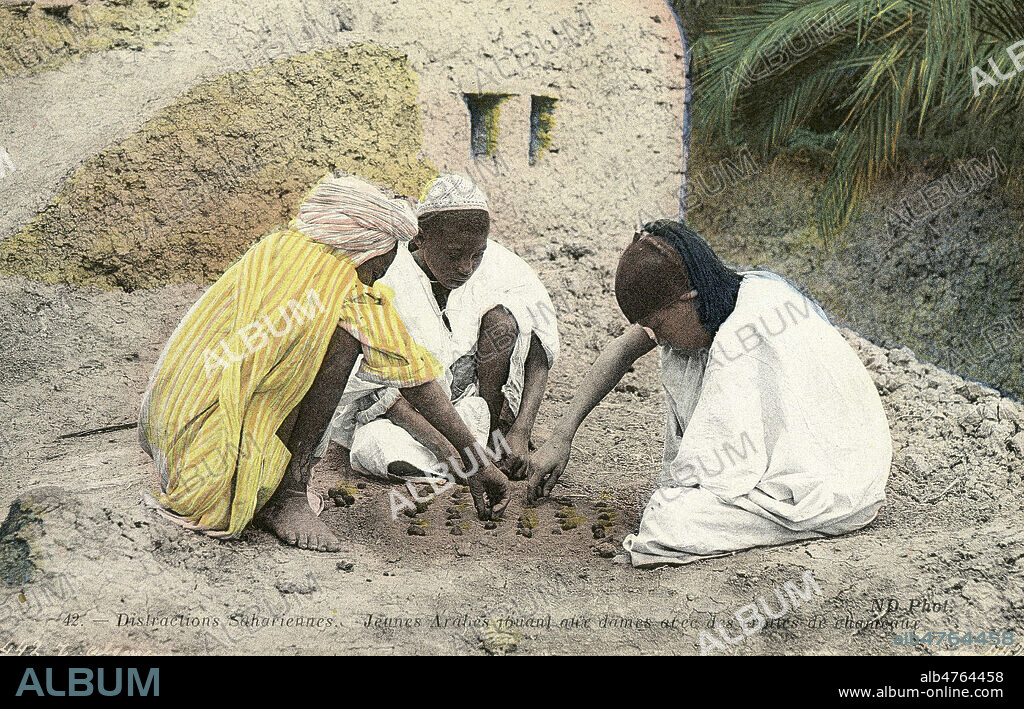 'Distractions sahariennes. Jeunes arabes jouant aux dames avec des crottes de chameaux'. Photographie anonyme pour une carte postale vers 1910. Credit : Collection IM/KHARBINE-TAPABOR.