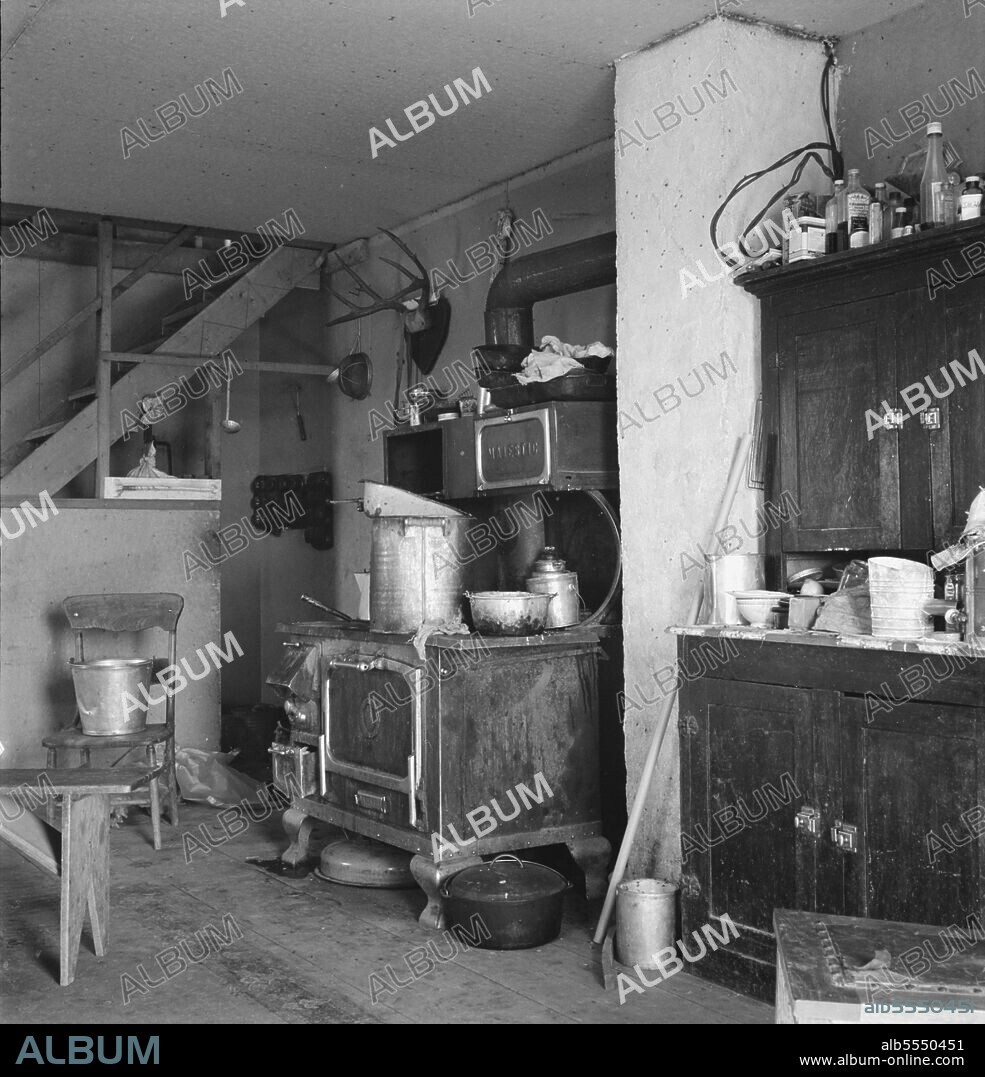 DOROTHEA LANGE. Another corner of the Soper kitchen. Willow Creek area, Malheur County, Oregon. [Note partly panelled in staircase; kitchen range; flies on container on floor].