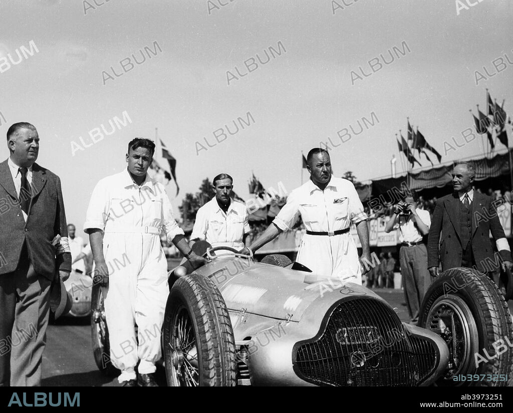 Alfred Neubauer with Mercedes car at the Start of the Italian Grand Prix, Monza, 1938. Neubauer, extreme left, accompanies the car of Caracciola as it is pushed into position on the starting grid. The car finished third. In 1926, Neubauer took over as manager of the Mercedes-Benz racing team, bringing in many innovative practices and presiding over its many successes until 1955. The company pulled out of racing in 1955 after one of their cars was involved in a disastrous crash at Le Mans, and Neubauer retired shortly afterwards.