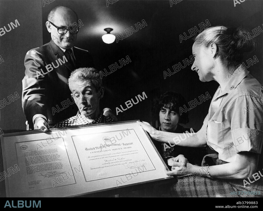 Woody Guthrie receiving a Conservation Service Award in 1966 from the U.S. Department of the Interior for his songs about the Columbia River. His son Arlo is seated to his left. Woodrow Wilson "Woody" Guthrie (July 14, 1912 - October 3, 1967) was an American singer-songwriter and musician whose musical legacy includes hundreds of political, traditional and children's songs, ballads and improvised works. Many of his songs are about his experiences in the Dust Bowl era during the Great Depression when Guthrie traveled with displaced farmers from Oklahoma to California. He died in 1967, at the age of 55, from complications of Huntington's disease. Arlo Davy Guthrie (born July 10, 1947) is an American folk singer. Like his father, Woody, Arlo often sings songs of protest against social injustice. He regularly performed with folk musician Pete Seeger, one of his father's longtime partners. His best-known work is "Alice's Restaurant Massacree", a satirical talking blues song about 18 minutes in length. His song "Massachusetts" was named the official folk song of the state in which he has lived most of his adult life.