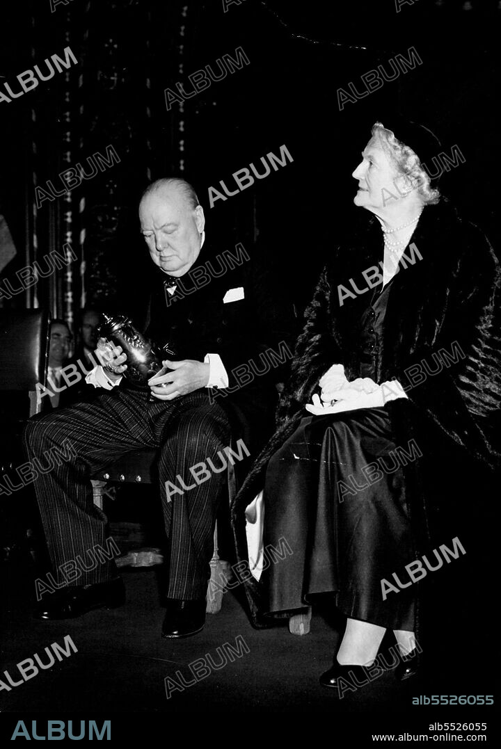 Gift For Sir Winston From Tory M.P's and Peers : With Lady Churchill beside him, Sir Winston Churchill is seen admiring one of the Queen Anne Silver Jugs after the presentation ceremony in the Royal Gallery of the house of Lord this evening. The gift was presented by Sir Anthony Eden on behalf of Conservative, Unionist and National Liberal Peers and Conservative, Unionists and National Liberal Members of Parliament, past and present.The last of several Birthday presentations to Sir Winston Churchill to mark his 80th. Birthday today, took place this evening in the Royal Gallery of the house of Lords, when, on behalf of Tory M.P.'s and Peers, Sir Anthony Eden presented the Prime Minister with two silver jugs, bearing the Churchill Arms. November 30, 1954.
