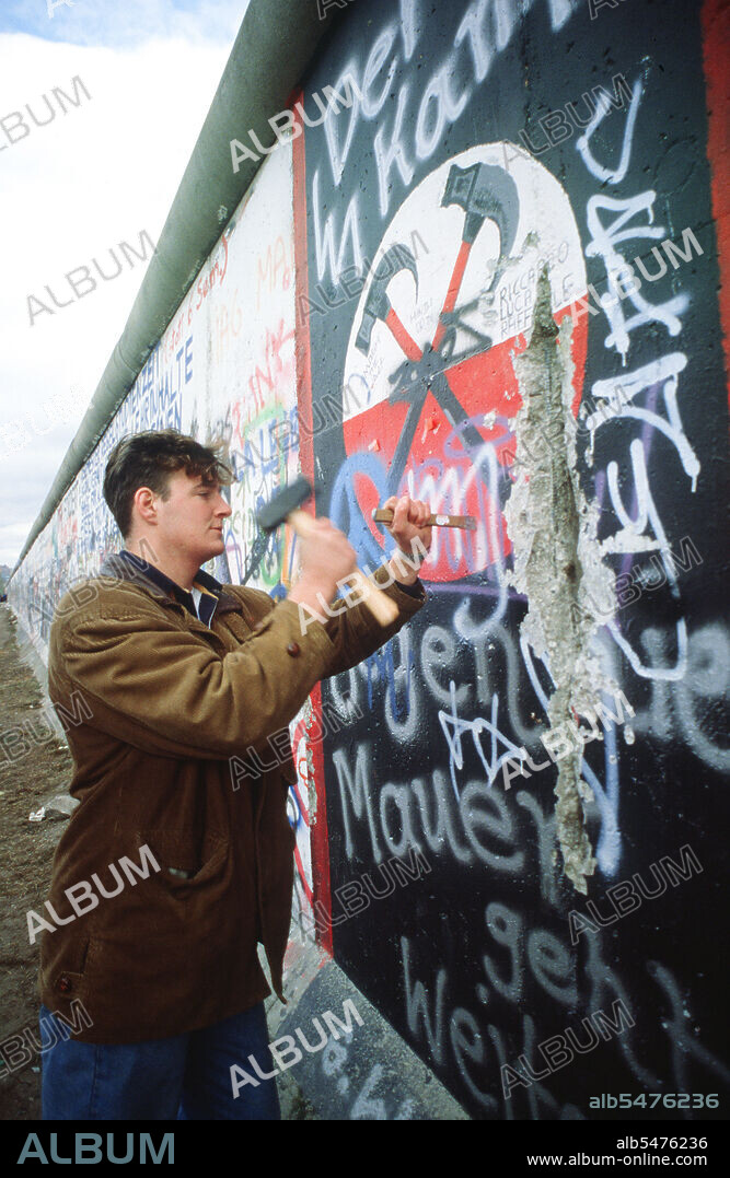 A West German man uses a hammer and chisel to chip off a piece of the Berlin Wall as a souvenir.  A portion of the Wall has already been demolished at Potsdamer Platz..