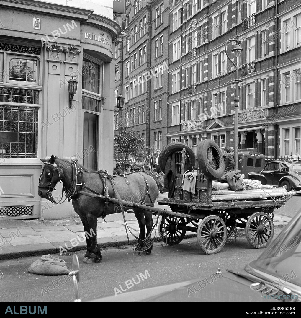 The Builders' Arms public house, Kensington, London, 1962-1964. A horse-drawn rag and bone cart standing on the road outside the pub at 1 Kensington Court Place, Kensington, with St Albans Mansions visible beyond.