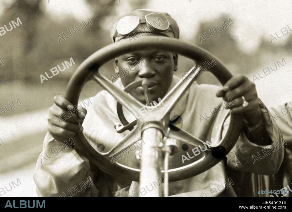 Jack Johnson looking through the steering wheel of his 90 horsepower Thomas Flyer automobile, John Arthur Johnson (March 31, 1878 - June 10, 1946) was the first African-American world heavyweight boxing champion (1908-15). He had a unique fighting style, which was not customary to boxing during this time. He would fight defensively, waiting for his opponents to tire out. He would continuously dodge their punches, and quickly strike back with a blow of his own. He often made his fights look effortless, but when pushed he could also display some powerful moves, and punches. He was an early example of the celebrity athlete in the modern era, appearing regularly in the press and later on radio and in motion pictures. On June 10, 1946, he died in a car crash after racing angrily from a diner that refused to serve him. He was 68 years old. During his boxing career, he fought 114 fights, winning 80 matches, 45 by knockouts. He was inducted into the Boxing Hall of Fame in 1954, and is on the roster of both the International Boxing Hall of Fame and the World Boxing Hall of Fame. Photographed by Louis Van Oeyen, September 6, 1910.