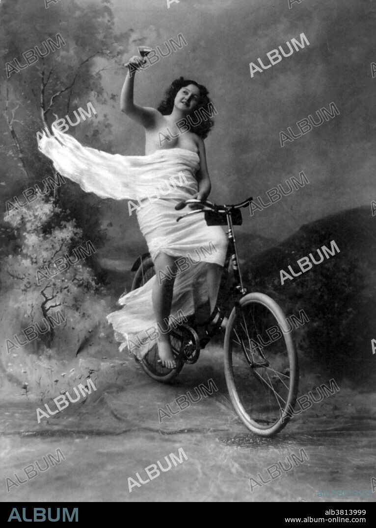 Entitled: "Queen of the wheel" shows studio portrait of a partially nude young woman, dressed in white flowing material, sitting on a bicycle, holding a glass of wine. Photographed by the Rose Studio, 1897. RisquÃ© photography is material that is slightly indecent or liable to shock, especially as sexually suggestive.
