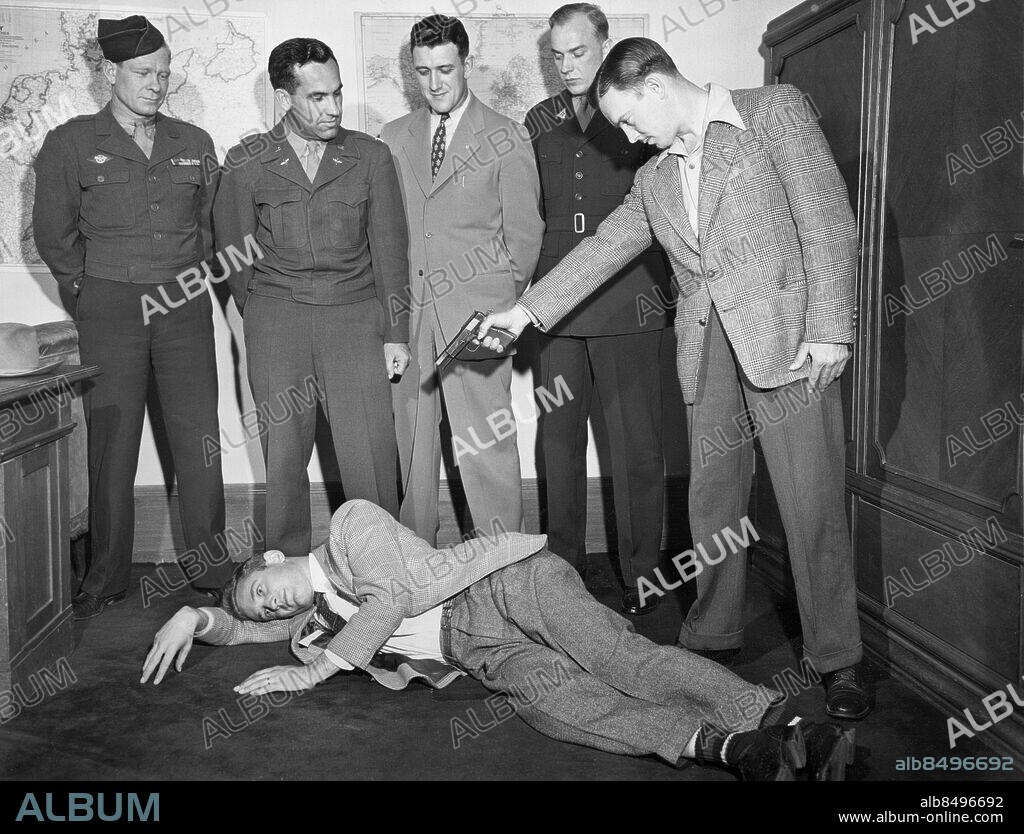 Orig. bildtext... TRACKING DOWN PERPETRATORS OF THE MALMEDY MASSACRE. Wiesbaden, Germany. These ex-gis have returned to Germany to testify against members of the first S.S. Panzers who have been uncovered from prisoner of war camps throughout Europe through the relentless efforts of the U.S. war crime branch. They are wanted for participation in the infamous Malmedy massacre. Kennethy Kingston of Allentown, Pa., on the floor demonstrates how an SS man fired two shots into his helmet, one just missing the top of his head and other grazing his upper lip. Carl B. Daub of Colebrook, Pa., takes the part of the S.S. man. L. to R. back row are, Samuel Dobyns of Sandusky, O. Lt. Col. Homer B. Crawford of Oklahoma City who is connected with the war crimes branch; Kenneth Ahrens of Eire, Pa., and Homer D. Ford of Leeton, Mo. The five former gis represent the 13 who escaped death by playing dead. The trial is to start the last of this month. Anm. Malmédy - stad i Belgien Efterkrigstiden Sikta Pistoler Åskådare Offer CD189 sites: TYSKLAND ;USA* ;WIESBADEN.
