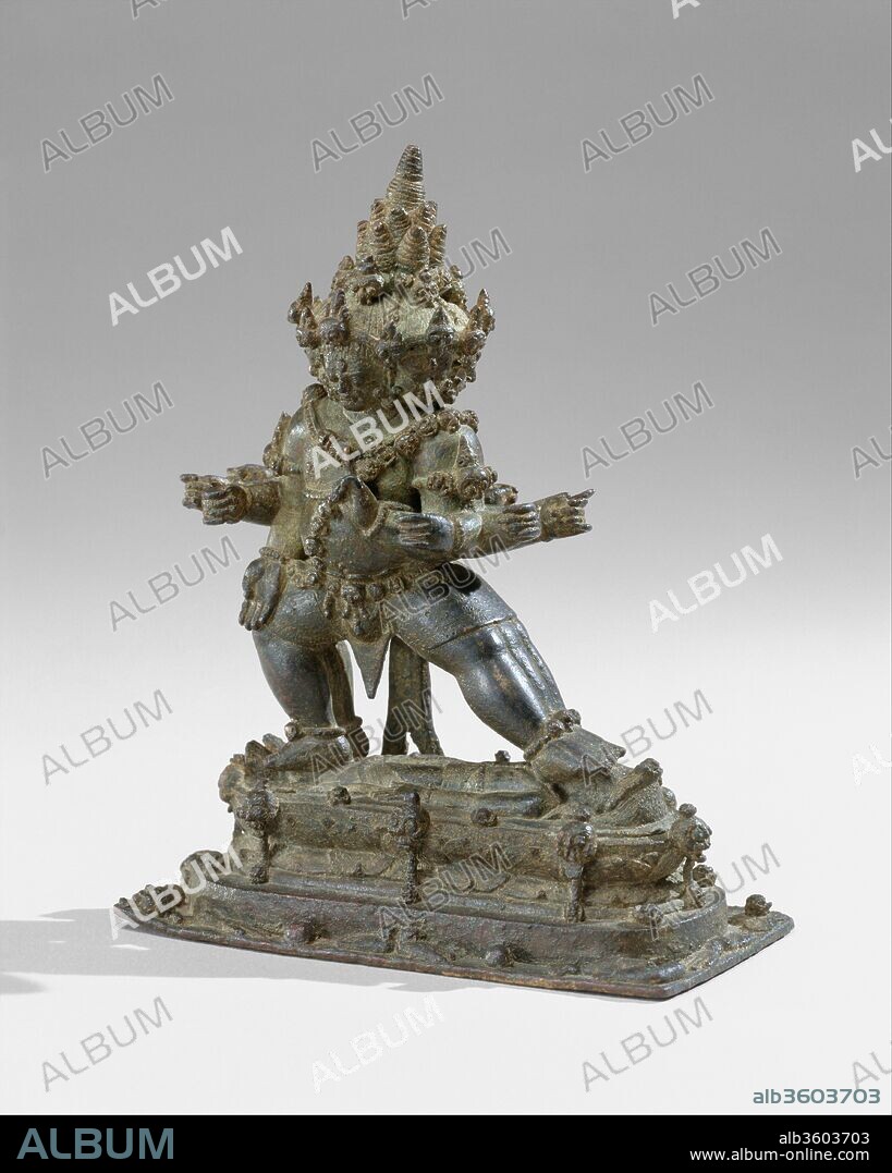 The Buddhist Guardian Mahabala. Culture: Indonesia (Java). Dimensions: H. 6 1/2 in. (16.5 cm). Date: 11th century.
According to certain traditional programs of Esoteric Buddhist iconography, Mahabala, similar to Yamantaka, is the conqueror of the lord of death and, by extension, of death itself. As a guardian of the faith (dharmapala), he is depicted as a fierce deity, shown here trampling a prostrate male, perhaps signifying death.
The powerful, corpulent protector adopts the aggressive stance of pratyalidha, a posture often used by figures trampling foes. His lowered right hand is in the boon-granting gesture and his raised left is in a sign of warning or menace. Mahabala is depicted with six heads, six legs, and twelve arms. Of the six faces, only one is pacific; the rest are wrathful, fanged, and terrifying. All of the heads wear diadems of skulls, and the deity wears a matching necklace and a sacred thread composed of skulls alternating with lotuses. Mahabala's hair is a series of spiraling conical forms, which heighten the sense of a great pyramidal mass being supported by the shoulders.
Mahabala frequents cemeteries, and his necropolitan associations--torsos, limbs, skull bones, and flayed skin--are graphically depicted around the base of the sculpture. Amid this grisly reminder of mortality, one macabre smiling head appears on the side of the base.
