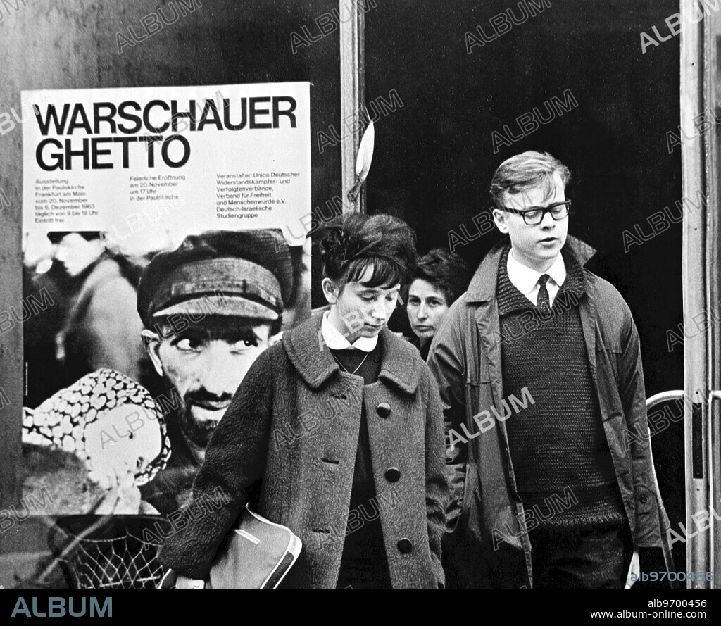 " Warsaw Ghetto " exhibition . Frankfurt , Germany ; Grim - faced, this young boy and girl walk from the " Warsaw Ghetto " exhibition , which opened here this week when pictures of wartime atrocities by the Nazis went on show to the public . The opening date of the exhibition , which is to tour every major German city , was chosen as 20 November , an annual German day of prayer and penance . Visitors are give brochures written by prominent ex - captives , aimed at preventing the lesson of the exhibition being forgotten at the hall door . 22 November 1963.