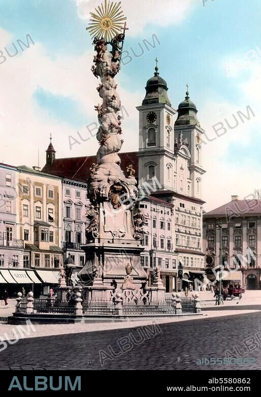 Linz (Österreich), Hauptplatz. Ansicht mit Dreifaltigkeitssäule (1723 geweiht; Entwurf: A.Beduzzi); dahinter der Alte Dom / Jesuitenkirche (1669-78 erbaut von P.F.Carlone). Foto, koloriert, um 1920.