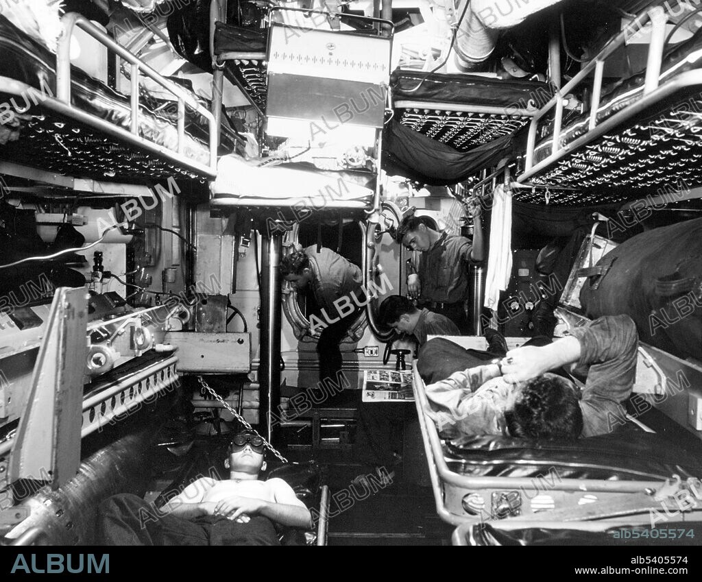 Unidentified submarine berthing space. Enlisted crewmen in the forward torpedo room of the boat during WWII. Note men in berths, torpedo stowed at left with man under sunlamp nearby, and small compartment door flanked by shafts for raising and lowering sound heads. Doorway leads to officers' country. (cropped and cleaned).